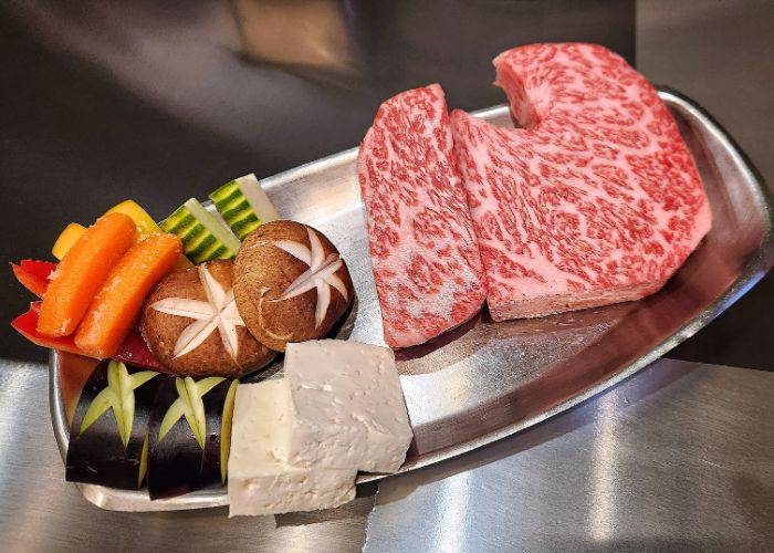 Raw slices of wagyu beef and vegetables waiting to be cooked on a silver tray at Tor Road Steak Aoyama.